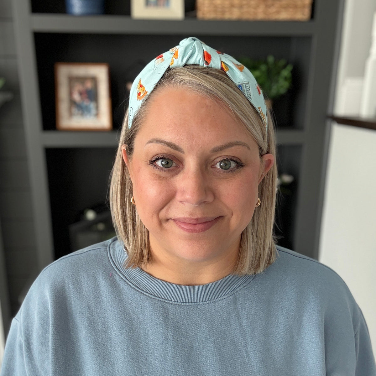 Woman wearing a light blue sweatshirt with a floral headband in an indoor setting.