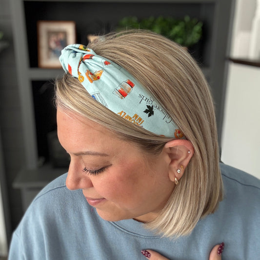 Woman wearing a headband with a pattern, sitting in a room with shelves and plants.