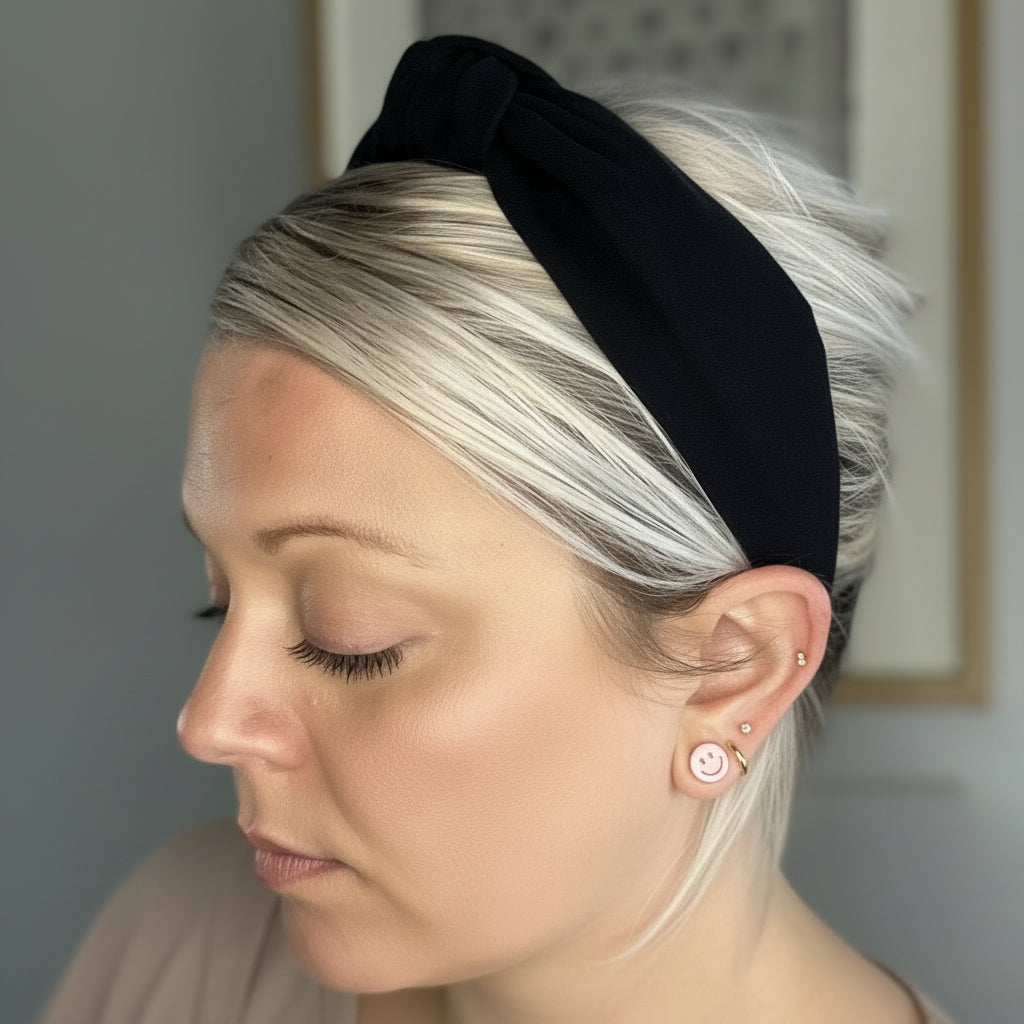 Person with black headband and earrings against a neutral background