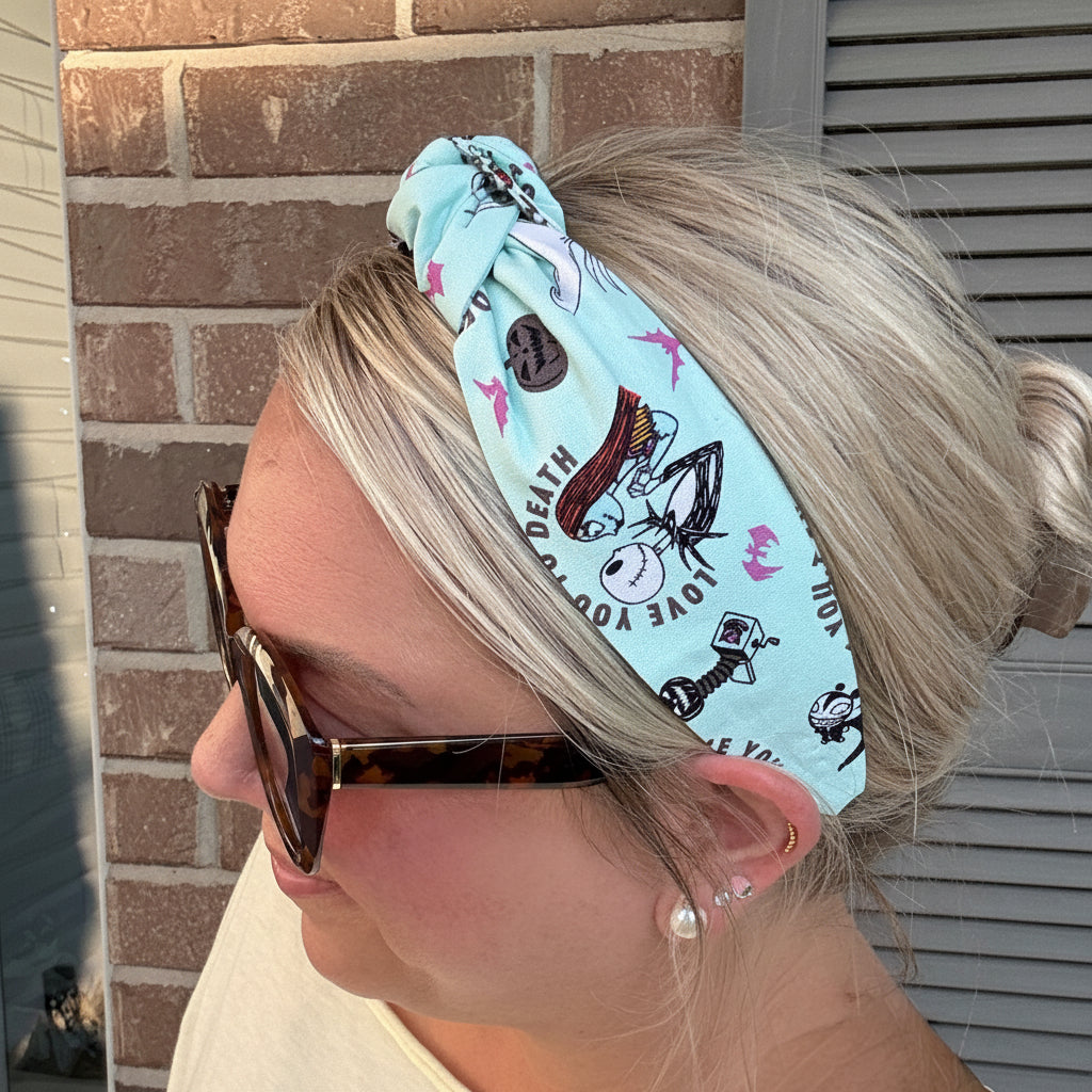 A woman wearing a light blue fabric headband with a printed cartoon character pattern and a brown button closure, shown in profile against a brick wall background.