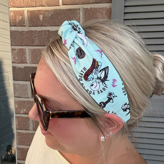 A woman wearing a light blue fabric headband with a printed cartoon character pattern and a brown button closure, shown in profile against a brick wall background.
