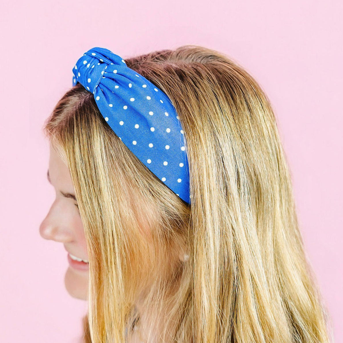 Woman wearing a blue polka dot headband against a pink background