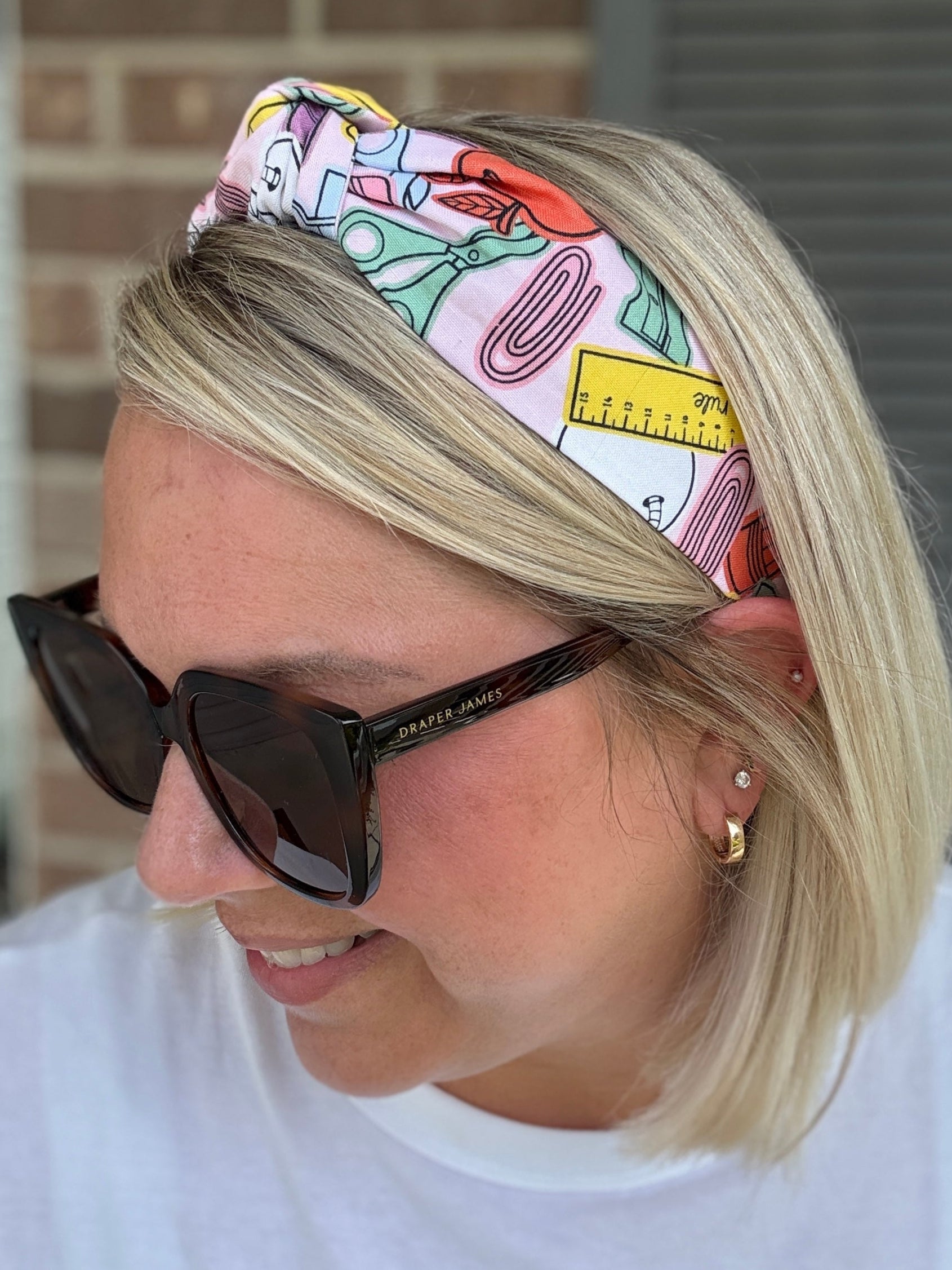 Woman wearing a colorful headband and sunglasses with a brick wall background