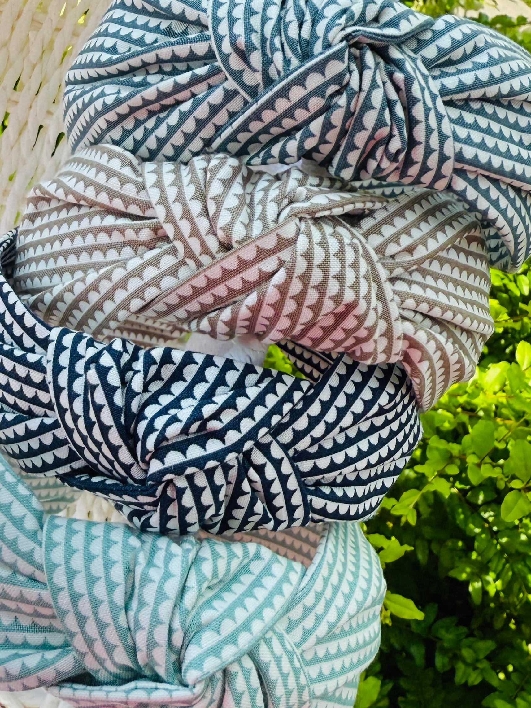 Stack of patterned headbands on a white chair with green foliage in the background